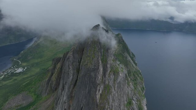 Drone footage of Segla rocky mountain and a lake behind clouds on Senja Island in Norway