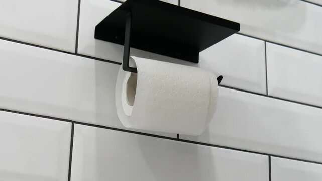 Close-up of male hands unrolling toilet paper roll and tearing off a bit