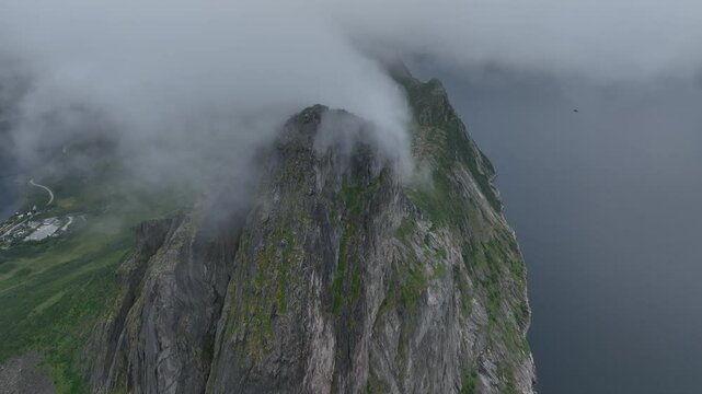 Breathtaking drone shot of Segla rocky mountain and a lake behind clouds on Senja Island in Norway