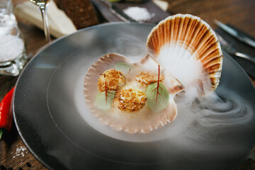 Grilled scallops served in a shell with avocado mousse and microgreens. Elegant seafood dish presented with dry ice smoke. Gourmet cuisine in a fine dining restaurant