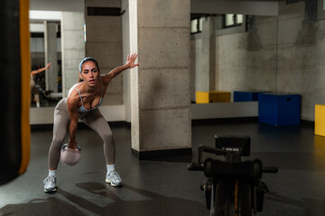 Determined hispanic sportswoman recording online workout session with kettlebell in modern gym, promoting healthy lifestyle and fitness training during social distancing