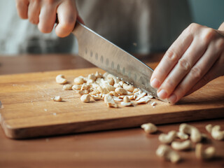 Female hands chopping cashew. Close up shot of process crushing raw unroasted cashew with large knife on wooden cutting board. Shallow DOF. Selective focus