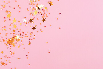 Shiny golden stars and crystals confetti on a pink background. Festive concept with copy space. Selective focus.