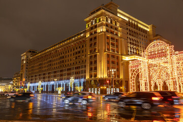Naklejka premium A large historical building in Moscow with festive illumination at night. A city street at dusk with passing cars. Car traffic at night. Moscow at night.