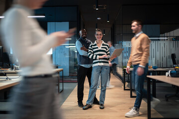 A confident woman in formal business attire, holding a laptop, strides purposefully through a bustling, contemporary coworking space, with colleagues moving energetically around her, highlighting a