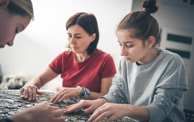Mother And Daughters Assembling Puzzles On A Table As The Family Spends Time Together