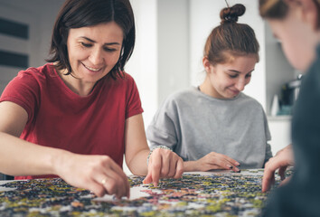 Fototapeta premium Mother And Daughters Assembling Puzzles On A Table As The Family Spends Time Together