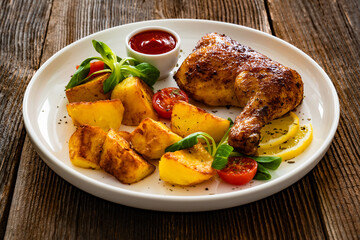 Oven roasted chicken thigh with fried potatoes and fresh salad on wooden table	