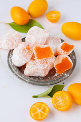Sweet kumquat delight or lokum closeup and fresh raw whole and sliced fruits with leaves on retro metallic plate on white marble table background.