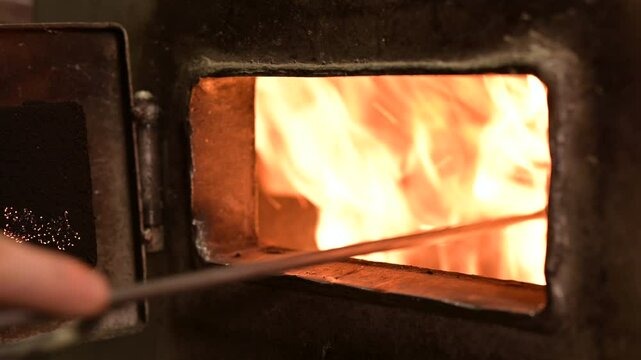 Open doors of an old firewood heater, adjusting firewood with fire iron. Heating residential building in cold winter with firebox