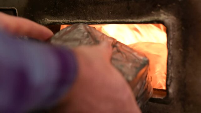 Heating building with rubbish. Man opens doors of firebox and puts rubbish bag with flammable wastes, burning wastes at home