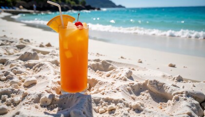 Orange drink with ice cubes, orange slice, and cherry on beach sand with turquoise sea and sunny weather