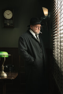 Portrait of a man in fedora and grey trench smoking near the window