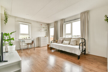 A bright and airy minimalist living room featuring a sofa, plants, and natural light streaming through large windows, providing a serene atmosphere.