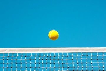 A Yellow Tennis Ball Hovers Above a White Net and Blue Sky