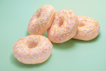 Donuts with white glaze and pink caramel crumbs on a green background
