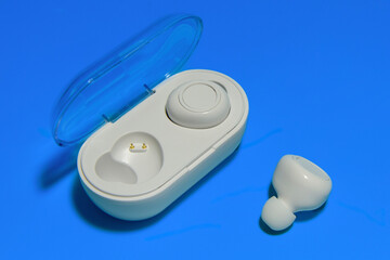 Bluetooth headphones in a white charging case close-up on blue