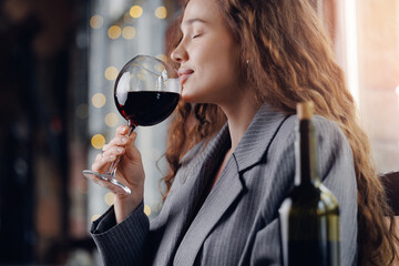 Sommelier young woman holds glass with red wine in restaurant, tests aroma and color