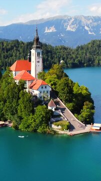 Aerial view of lake bled island with pilgrimage church of the assumption of maria on a sunny summer day with julian alps and bled castle in the background