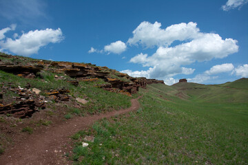A red sandstone path leads to the top of a beautiful hill set against a backdrop of blue sky and green grass