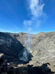 Dramatic volcanic crater with steam rising under bright blue sky, inspiring awe and natural wonder