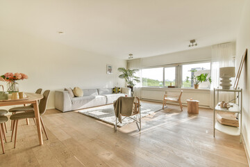 A beautifully designed modern living room featuring a cozy sofa, dining table, and large windows that bring natural light, creating an inviting atmosphere.