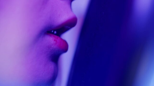 Close up of a female mouth and a black pop filter in front of a microphone. Macro shot of red lips speaking for a voice recording in a purple studio. The concept of modern audio recording and hobby