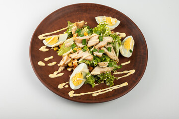 Delicious Caesar salad with grilled chicken, boiled eggs, fresh lettuce, corn and creamy dressing on a brown clay plate. A healthy and tasty dish for a perfect lunch