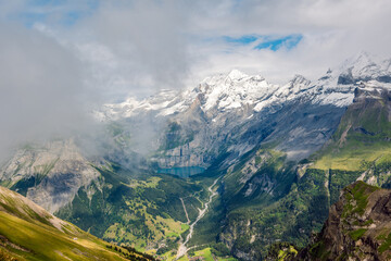 Mixture of clouds with a mist over a picturesque alpine valley and blue mountain lake, Oeschinen Lake, Berner Oberland, Switzerland.