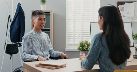 Disabled man dressed in smart blue striped shirt sits at desk in corporate office in wheelchair, he...
