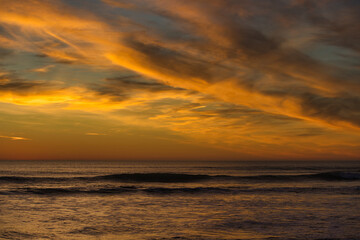 Sunset at sea with high, reddish clouds.