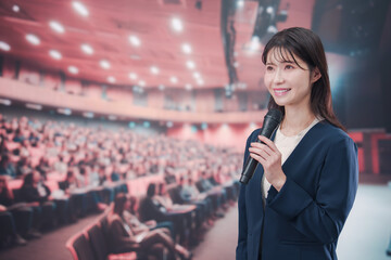 大勢の聴衆が集まるホールで司会をする若い女性