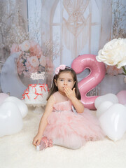 Generated A little girl in pink clothing celebrates in a fairy-tale setting with pastel decorations, a large pink balloon in the shape of a two, and white flowers, radiating joy and innocence.