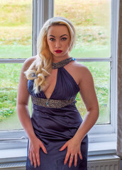 Beautiful woman in blue evening dress in front of window staring at observer