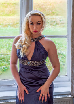 Beautiful woman in blue evening dress in front of window staring at observer