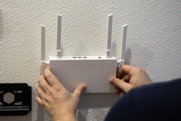 An individual is installing a wireless router with antennas on a wall to improve internet access...