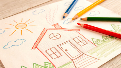 A child’s drawing of a house, surrounded by the color pencils used to create it.  