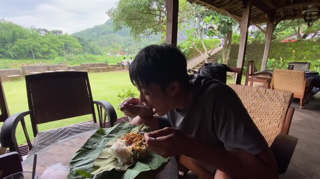 An indonesian man is eating Sego Berkat, a javanese traditional dish contains of white rice and various mixed side dishes.