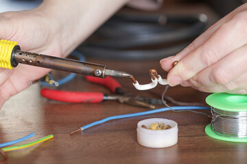 Woman Solders cooper wires with a soldering iron. Soldering, maintenance and repair work at home