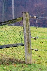 Broken wire mesh fence leaning on weathered wooden post in rural landscape