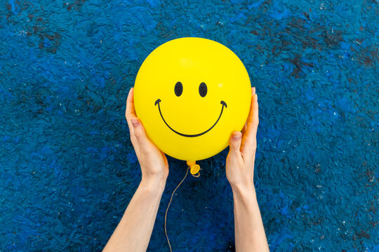 Happy smiling yellow balloon in hand. Happiness emotions concept