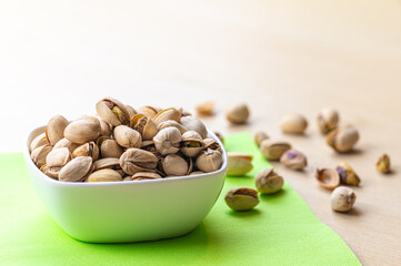 Pistachios in shell, in white bowl, on green napkin and wooden surface. Properties and uses of pistachio.