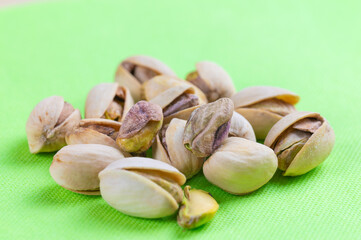 Pistachios in shell, in white bowl, on green napkin and wooden surface. Properties and uses of pistachio.