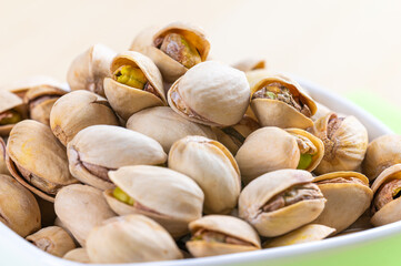 Pistachios in shell, in white bowl, on green napkin and wooden surface. Properties and uses of pistachio.