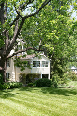 white summer house immersed in greenery with a large green lawn.