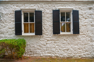 Two antique windows with shutters in the wall of an old white stone house.