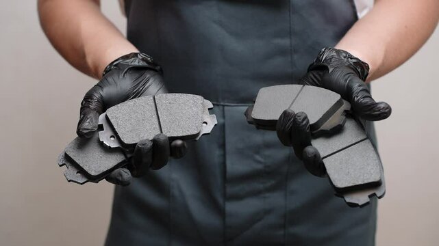 Auto mechanic in overalls holding four brake pads in hands showing them, close-up, preparing to replace them. Concept of maintenance, serviceability of car brake system.