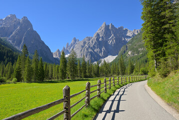 Val Fiscalina road leading through the Dolomites mountains. Paved road winding through a green valley with a wooden fence and dramatic peaks. © Tomherkules