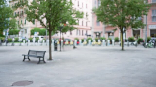 Blurry street scene in la spezia with bokeh effect featuring empty benches and defocused trees lining the pedestrian area in italy's scenic town square.