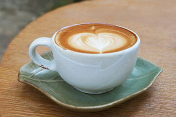 A cup of cappuccino coffee with heart shaped latte art isolated on wooden table